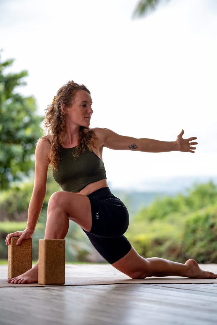 Posture de yoga en fente avec blocs, au bord d'une terrasse tropicale